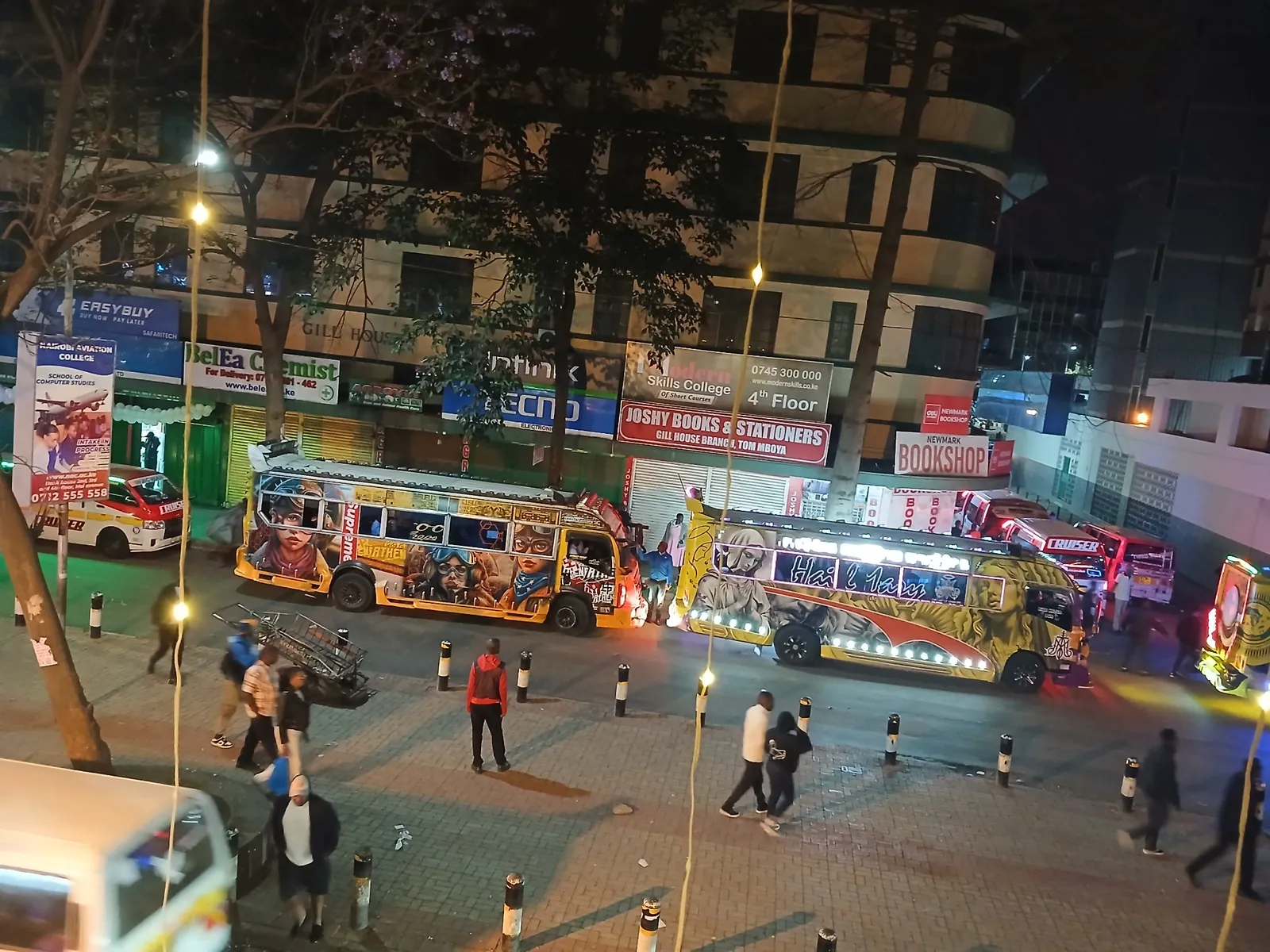 Matatus parked outside shops, colleges and a bookshop on Tom Mboya Street at night